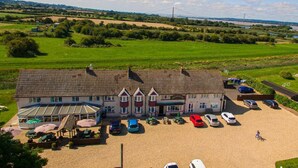 A large building with a tiled roof, a covered outdoor seating area, and a parking lot with several cars. - The Haven Inn (Barrow upon Humber)