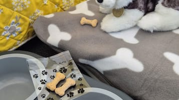 A dog bed with bone-shaped treats, a water bowl, and a food bowl on a gray tray.