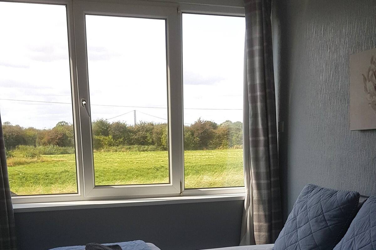 A bedroom with a bed, a window, and a view of a green field.