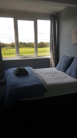A bedroom with a bed, a window, and a view of a green field. - The Haven Inn (Barrow upon Humber)
