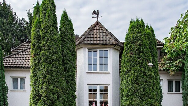 A two-story building with a symmetrical facade, a central entrance with double doors, and a weather vane on the roof. - Gästehaus Villa Sulmana (Neckarsulm)