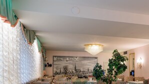 A dining area with tables set for tea service, chairs with patterned upholstery, a chandelier, and a large cityscape painting on the wall. - Gästehaus Villa Sulmana (Neckarsulm)