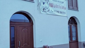 Een gebouw met een bord waarop 'B&B La Vecchia Osteria' en een telefoonnummer staan. Er zijn twee houten deuren en een raam met luiken.