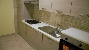 Een keuken met een gasfornuis, spoelbak en vaatwasser. Het heeft lichtgekleurde kastjes en een betegelde achterwand.