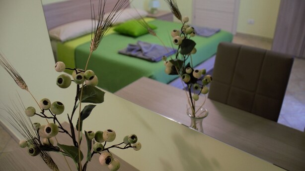 Een slaapkamer met een groene sprei, een bruin hoofdeinde en een spiegel die de kamer weerspiegelt.