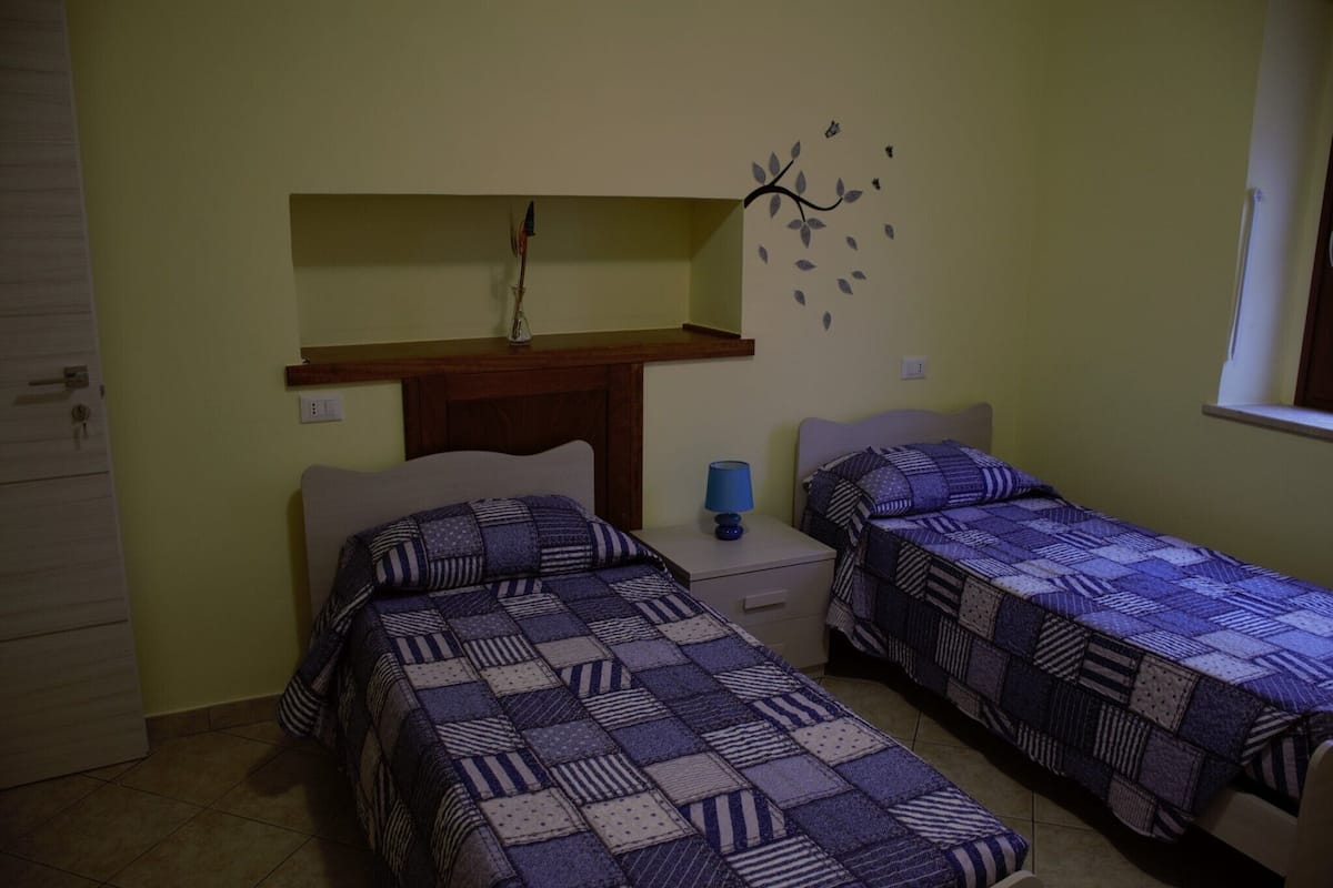 Une chambre avec deux lits, une table de chevet, une étagère avec une lampe et un élément décoratif mural.
