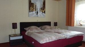Een slaapkamer met een bed, twee bedlampen, een raam met gordijnen en een schilderij aan de muur.