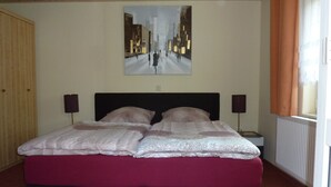 Een slaapkamer met een groot bed, twee bedlampen, een schilderij aan de muur en een raam met gordijnen.