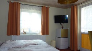 Een slaapkamer met een bed, een televisie op een standaard, een radiator en gordijnen.