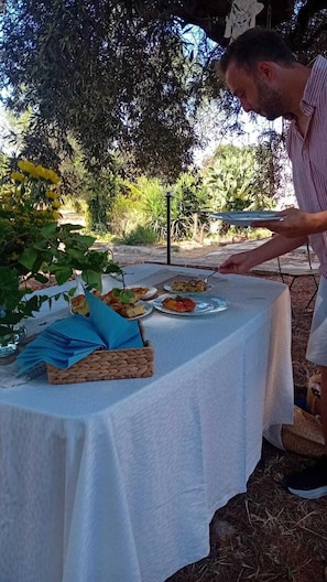 Mesa de comedor al aire libre con mantel blanco, rodeada de follaje y árboles.
