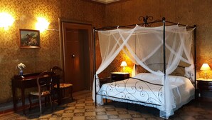 Un lit à baldaquin, un bureau en bois avec une chaise et deux lampes de chevet.