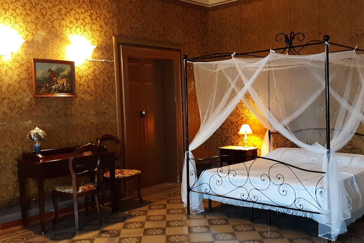 Un lit à baldaquin, un bureau en bois avec une chaise et deux lampes de chevet.