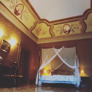 Habitación con cama bajo dosel, diseño ornamental del techo y dos lámparas de noche.