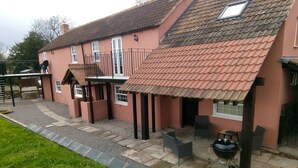A house with a sloped roof, a patio with outdoor furniture, and a barbecue grill. - Pershbrook Cottage & Garden on the River Severn. (Minsterworth)