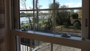 A window with a view of a lake, a wooden deck, and some greenery. - Pershbrook Cottage & Garden on the River Severn. (Minsterworth)