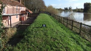 A riverside walkway with a building on the left and a wooden fence on the right. - Pershbrook Cottage & Garden on the River Severn. (Minsterworth)