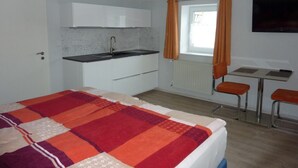 A compact room with a bed, a kitchenette, a small table, and two chairs. - Cozy apartment 5 (Zeulenroda-Triebes)