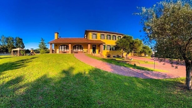 A two-story yellow building with a red roof, surrounded by a well-maintained lawn and a paved path leading to the entrance.