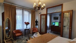 A hotel room with a large bed, a sitting area with two chairs, a vanity with a mirror, and a chandelier.