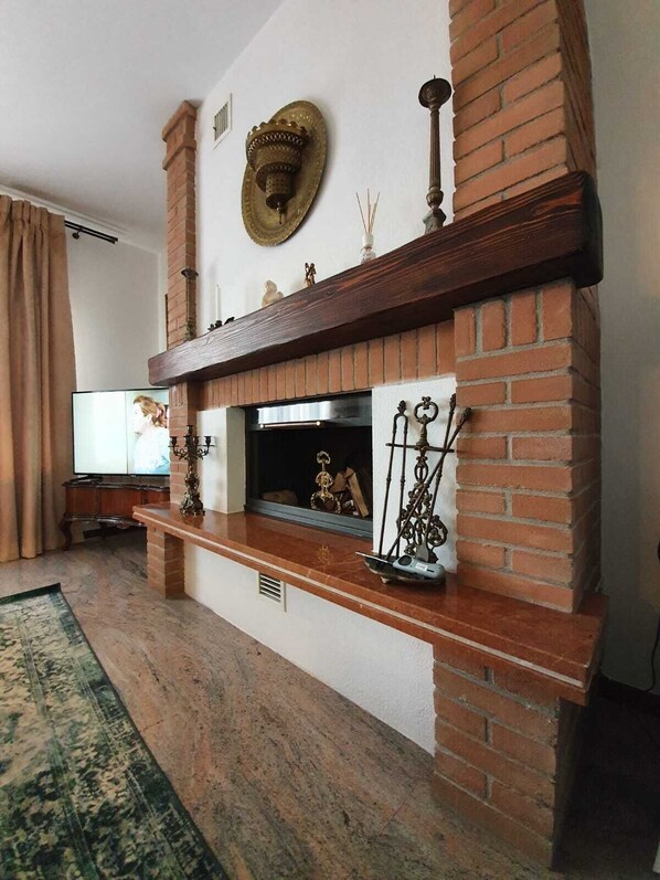 A living room with a brick fireplace, a television, and a decorative mirror.