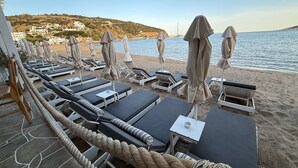 Un espace de détente aménagé au bord de la plage, avec des chaises longues et des parasols, offrant une vue sur la mer et sur une ville située sur une colline.