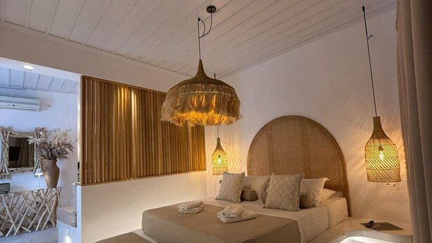 Une chambre moderne avec un grand lit, des lampes de chevet et un coin repas avec des chaises en osier.