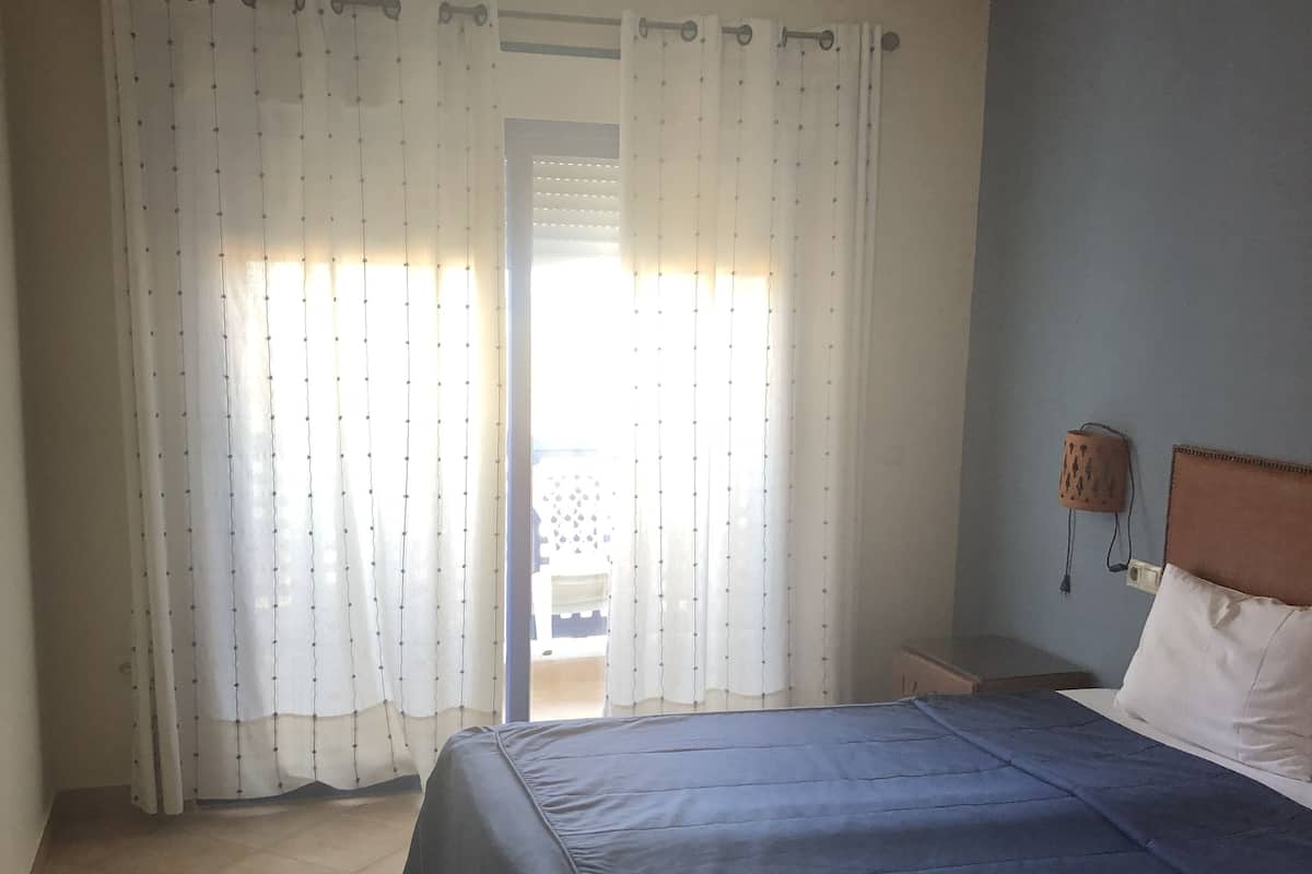 A bedroom with a bed, curtains, a nightstand, and a wall-mounted lamp.