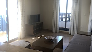 Una sala de estar con sofá, mesa de centro, televisor y balcón con cortinas.