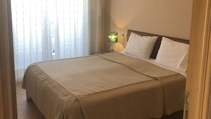 Una habitación de hotel con una cama grande, una lámpara de noche y un ventanal con cortinas.