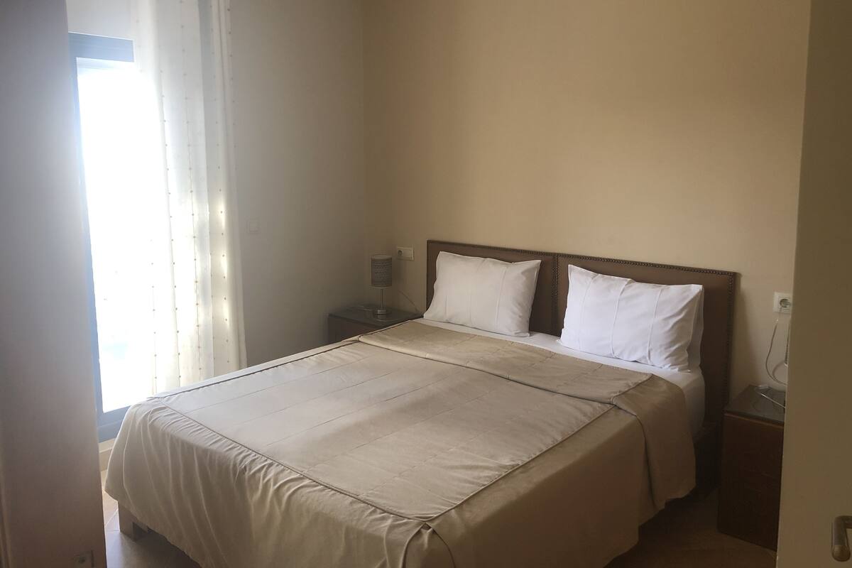 A bedroom with a bed, a nightstand, a lamp, and a window with curtains.