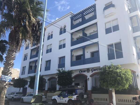 Un edificio de varios pisos con balcones, un letrero que dice 'Casa Garcia' y coches estacionados.