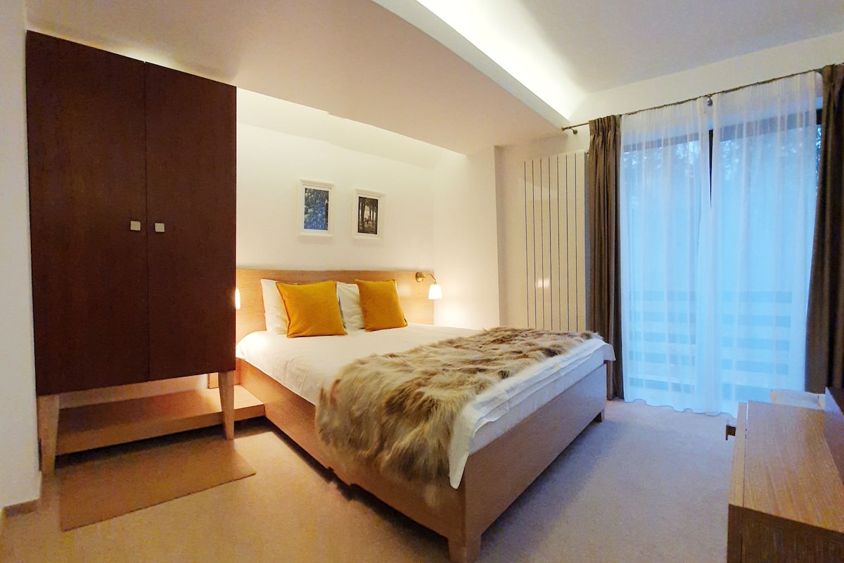 A hotel room with a bed, a wardrobe, a nightstand, and a window with curtains.