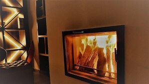 Een wandhaard met brandhout, een comfortabele bank en een geometrisch wandontwerp.