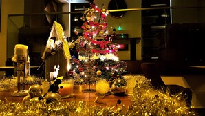 Een kerstboom met versieringen en lichtjes, een notenkraker en een kaars op een tafel.