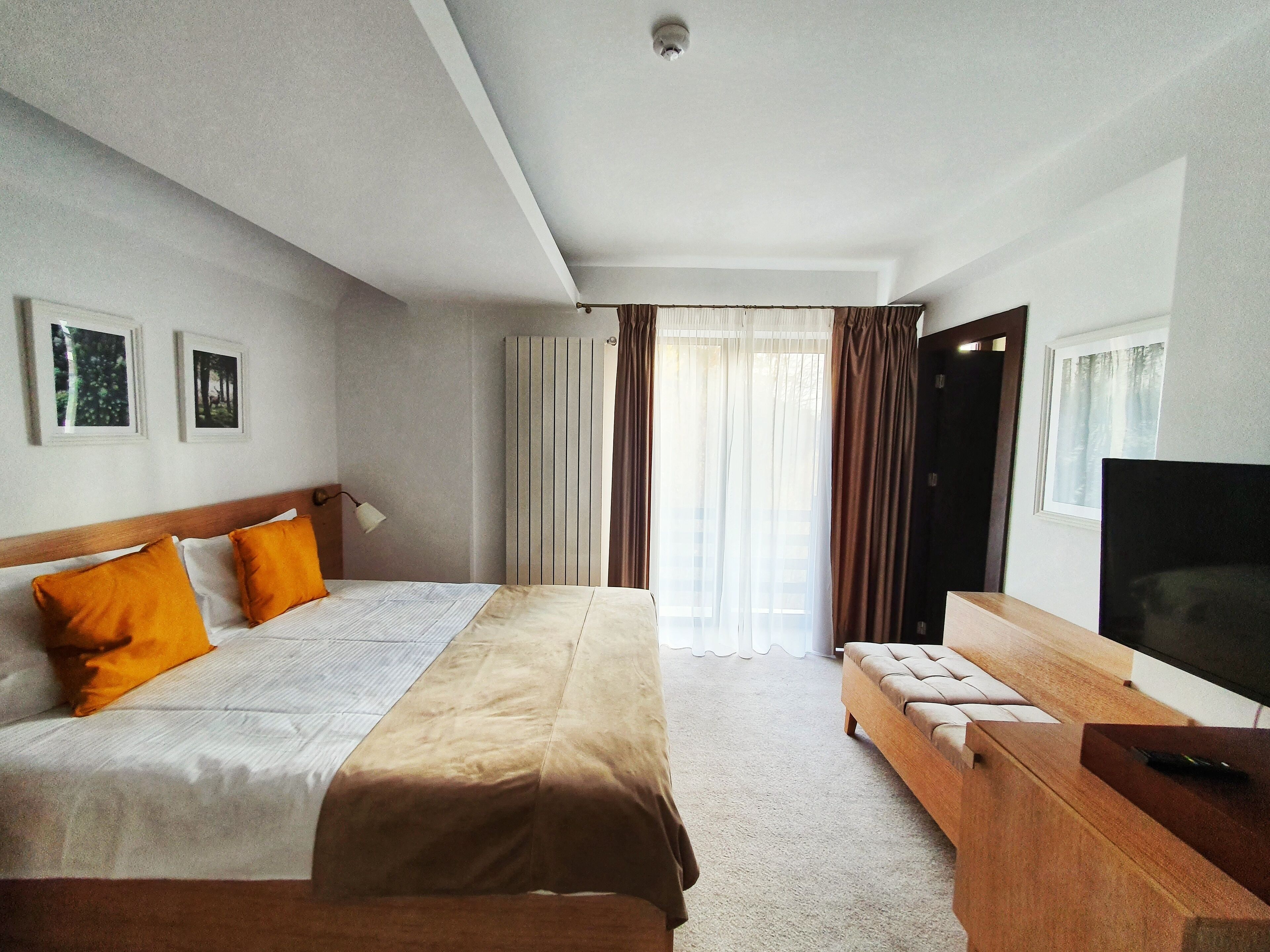 A hotel room with a bed, a TV, a desk, and a window with curtains.