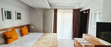 A hotel room with a bed, a TV, a desk, and a window with curtains.