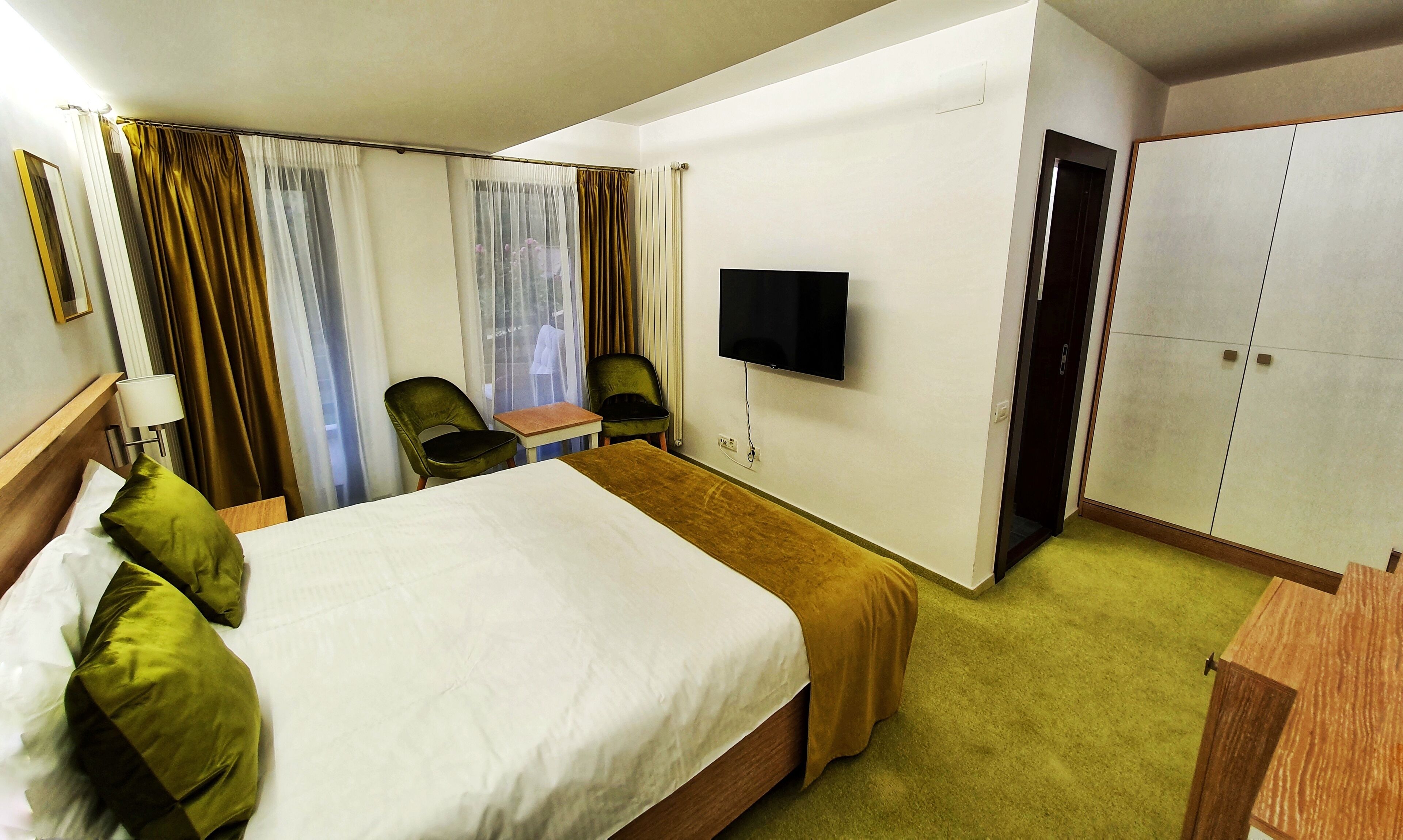 A hotel room with a bed, a desk, a chair, a television, and a wardrobe.
