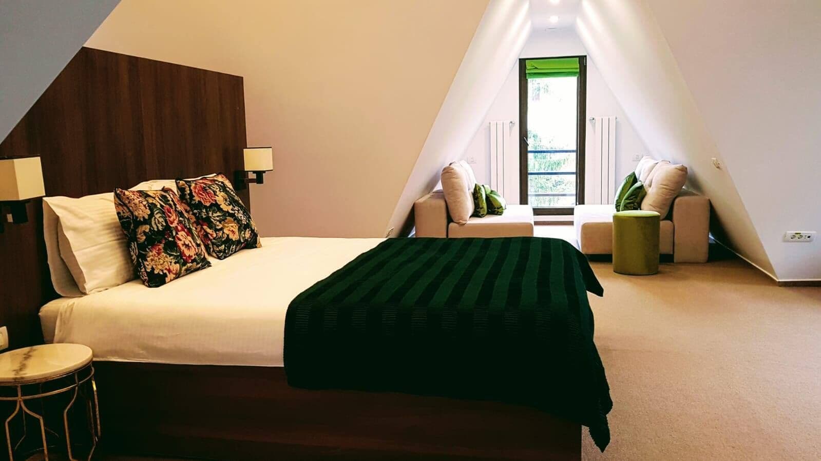 Ein Schlafzimmer mit Bett, Nachttisch, Lampe, Fenster und kleinem Tisch.