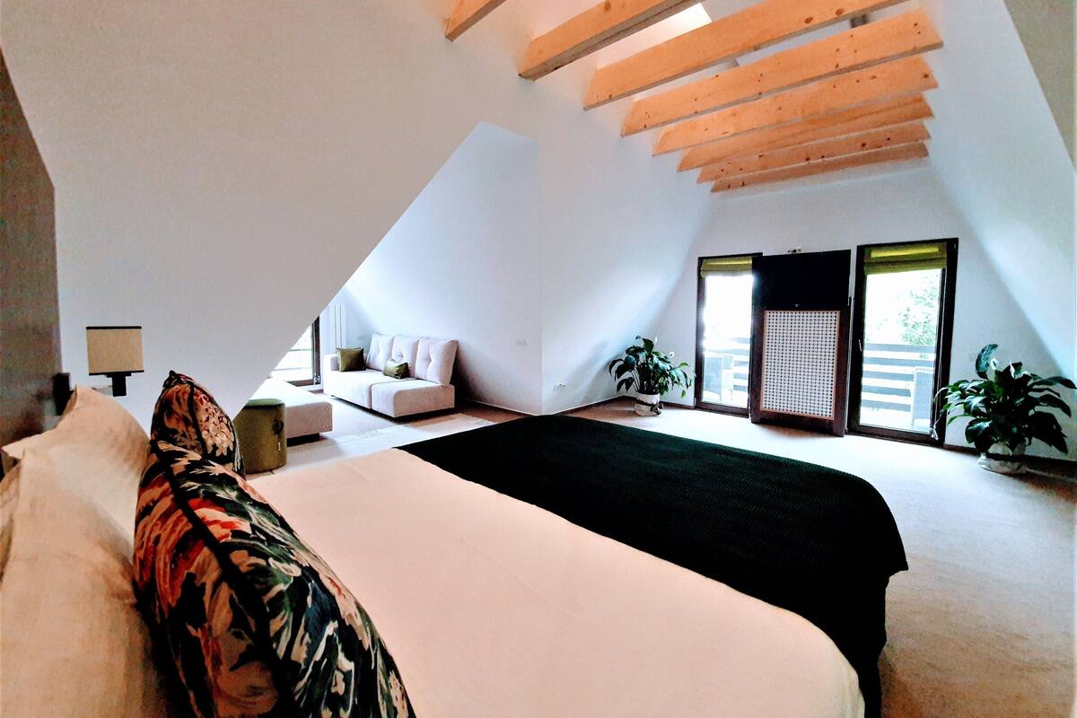 A bedroom with a large bed, a sofa, a desk, and a window with a view.