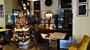 Een modern interieur met een kerstboom, een piano en een stadszicht door grote ramen.