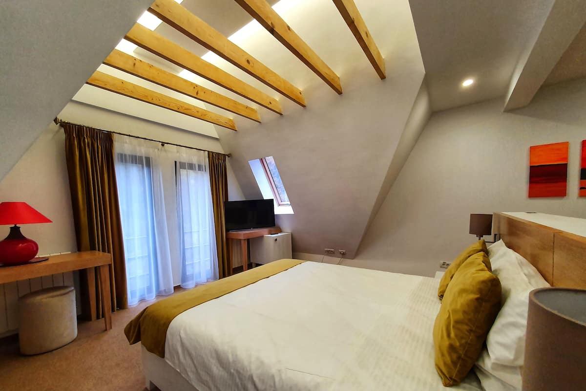 A bedroom with a sloped ceiling, a bed, a TV, and a desk.