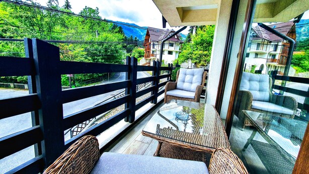 Een balkon met rieten meubilair, een glazen tafel en uitzicht op huizen en bomen.