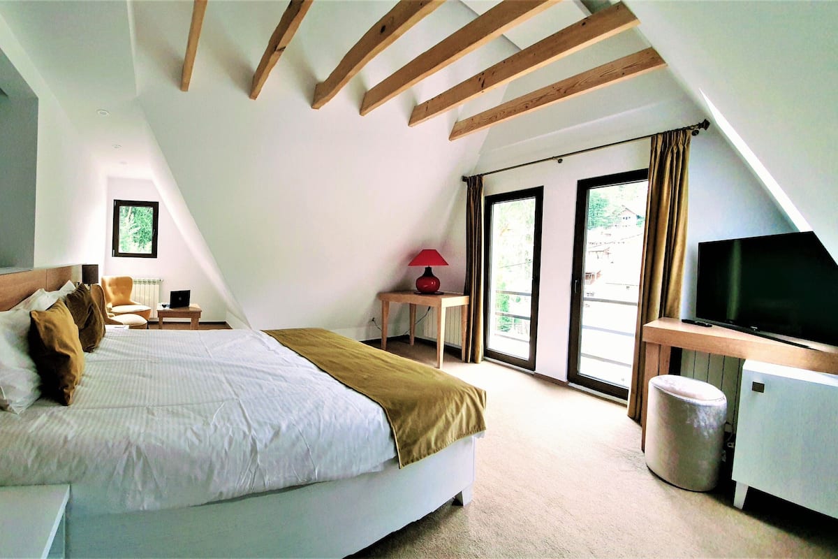 A bedroom with a bed, a desk, a chair, a TV, and a window.