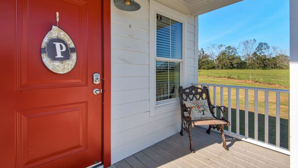 A red door with a 'P' sign, a bench with a floral cushion, and a view of a grassy field. - Porter's Cottage....Tiny Home Located At Stillwater Ranch (Laurel Hill)