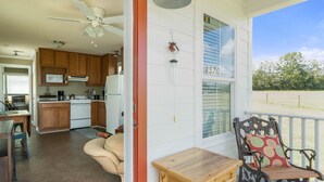 A spacious living area with a kitchen, a dining table, and a porch with a chair. - Porter's Cottage....Tiny Home Located At Stillwater Ranch (Laurel Hill)