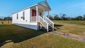 A white single-story house with a red door, a covered porch, and a wooden staircase. - Porter's Cottage....Tiny Home Located At Stillwater Ranch (Laurel Hill)