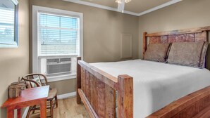 A bedroom with a wooden bed, a ceiling fan, a window with blinds, and a small table with chairs. - Porter's Cottage....Tiny Home Located At Stillwater Ranch (Laurel Hill)