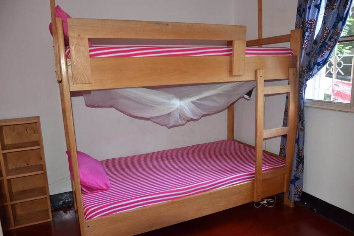 Un lit superposé avec un matelas rayé rose et blanc, un ciel de lit blanc et une échelle en bois.