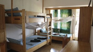 Une chambre de dortoir avec des lits superposés, une petite table et une fenêtre ornée de rideaux à motifs.