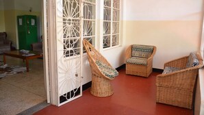 Une pièce avec des chaises en osier, un meuble vert et une porte blanche ornée de panneaux de verre décoratifs.